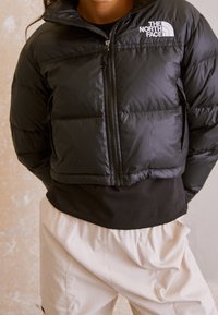 Svart puffjacka med frontdragkedja, hög krage och The North Face-logotyp. Har kviltade sektioner och en avslappnad passform.