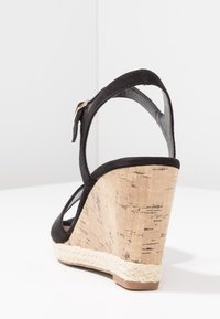 Černé semišové sandály na klínu s korkově strukturovanou patou, kotníkovým páskem a pleteným jutovým detailem podél spodní části. Design s otevřenou špičkou.