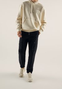 Kram hoodie med framficka och dragsko, tillsammans med svarta cargobyxor med två sidofickor, och lätta sneakers med texturerade sulor.