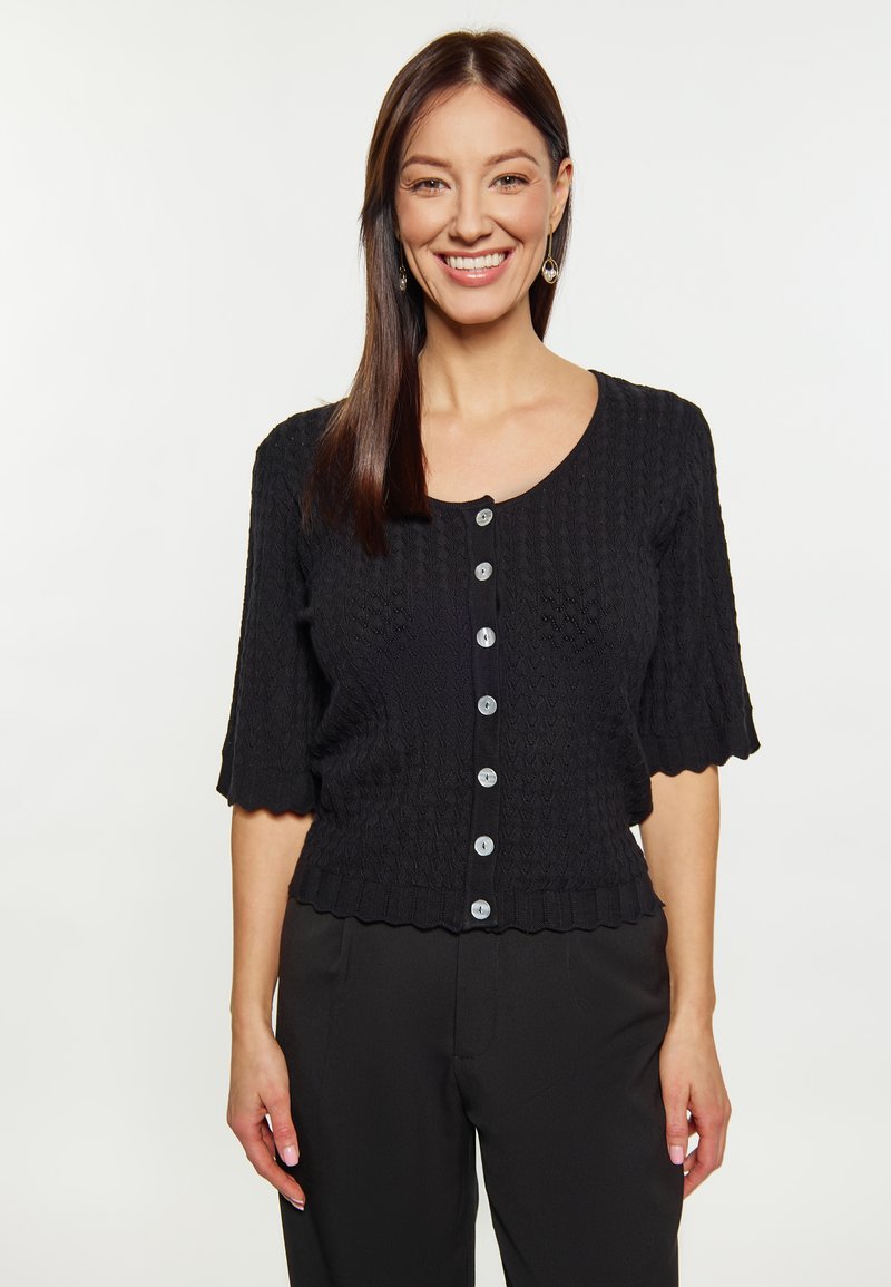 Cardigan nero a maglia con un motivo testurizzato, maniche corte e orlo a scallop. Presenta cinque bottoni di colore chiaro sul davanti.