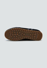 Sneaker nera con una parte superiore nera testurizzata, tre strisce scure e una suola in gomma marrone con battistrada circolare per una migliore aderenza.