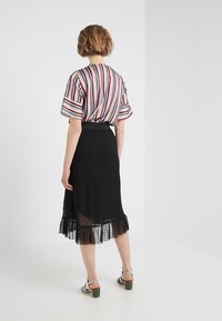 Mehrfarbige gestreifte Bluse mit kurzen Ärmeln, kombiniert mit einem schwarzen, transparenten Rock mit einem Rüschensaum und einem gerafften Bund.