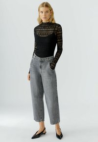 Schwarzes Spitzenoberteil mit langen Ärmeln und Blumenmustern, kombiniert mit hellgrauen, hochtaillierten, weit geschnittenen Jeans und schwarzen, spitzen Ballerinas.