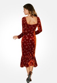 Czerwona sukienka z weluru, z długimi rękawami, kwadratowym dekoltem, kwiatowymi wzorami i rozkloszowanym dołem. Gładka tekstura z dopasowanym fasonem.