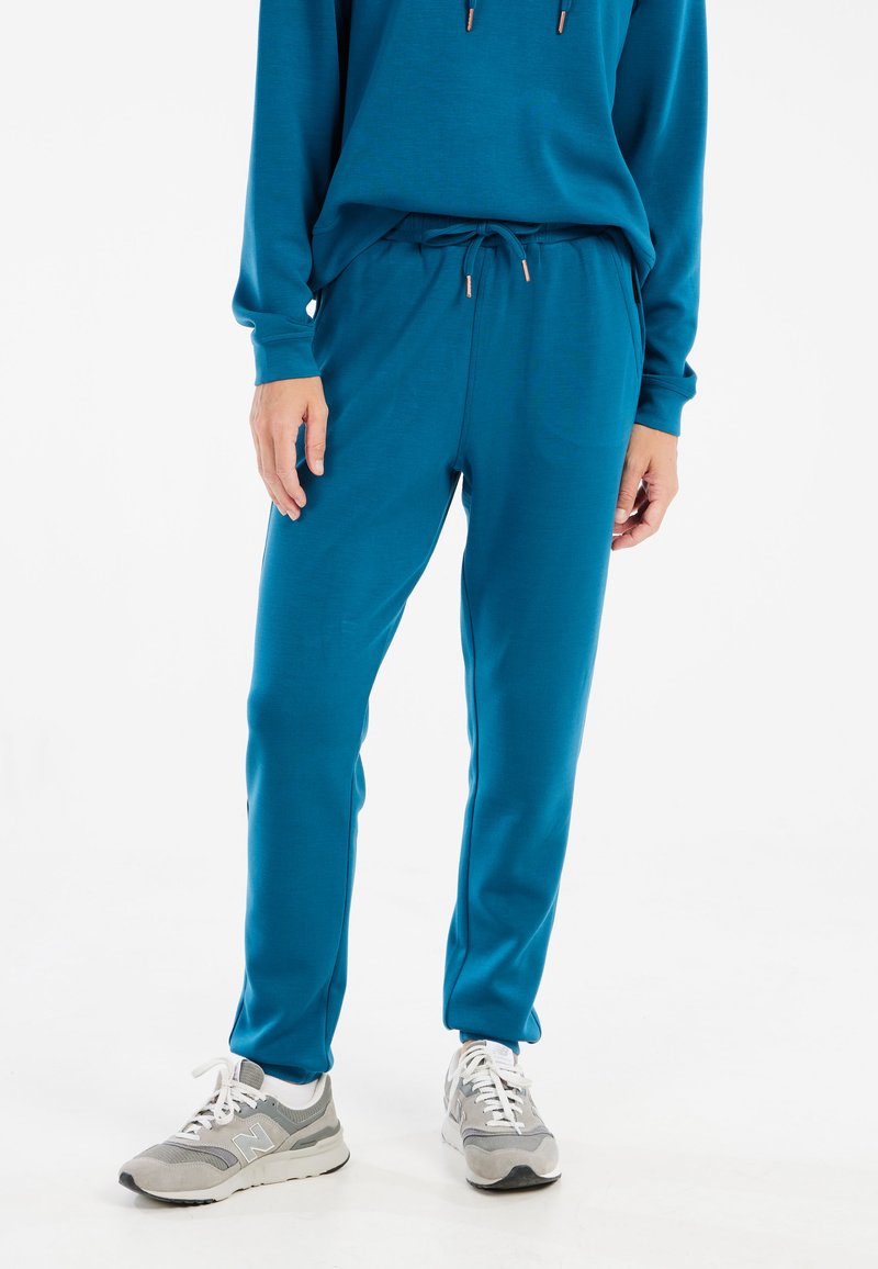 Turquoise sportoutfit bestaande uit een hooded top en bijpassende taps toelopende broek, gemaakt van zacht materiaal met trekkoorddetails en geribde boorden.