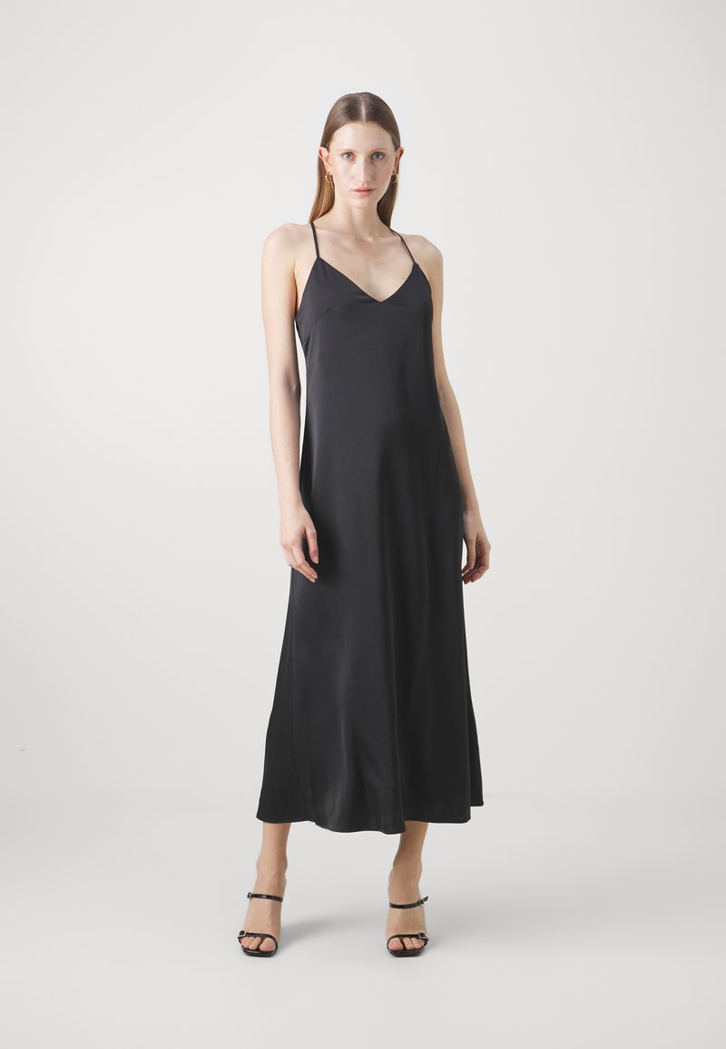 Abito in satin nero con scollo a V, spalline sottili e silhouette a lunghezza intera. Texture liscia e design minimalista. Décolleté neri con cinturini.