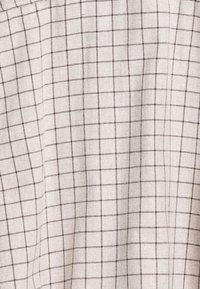 Licht beige stof met een geruit patroon in donkerbruin. De textuur lijkt geweven en zacht, met gelijkmatig verdeelde rasterlijnen.