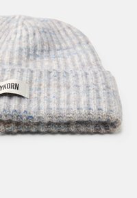 Gorro de malha cinza claro com textura canelada, apresentando pequenos pontos discretos em azul e bege e uma etiqueta com a palavra "KORN". Dobrada para um ajuste justo.