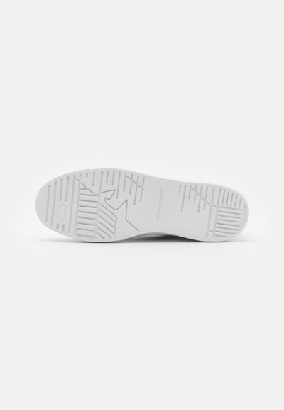 Vita sneakersula med en texturerad gummiyta med ribbor och spår för grepp; logotyp präglad nära hälen, platt profil.