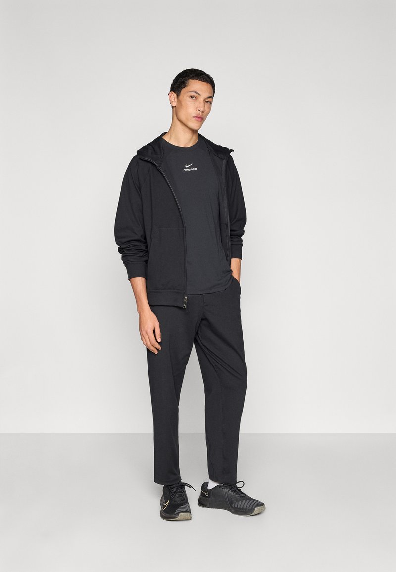 Black athletic outfit featuring a zip-up hoodie, short-sleeve t-shirt, and tapered pants, complemented by black sneakers with textured detailing.