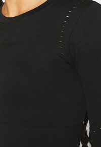 Top sportivo nero con scollo a girocollo, caratterizzato da sottili perforazioni sulle spalle e un tessuto testurizzato per la traspirabilità.