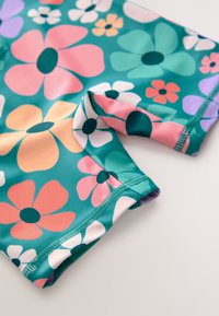 Mehrfarbige Badehose mit Blumenmuster in Türkis, mit großen pinken, violetten und weißen Blumen. Glatte Textur mit genähten Kanten und einem anliegenden Design.