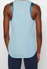 Débardeur sportif bleu clair avec une texture lisse, des larges bretelles et un ourlet incurvé. Présente une couture subtile au dos pour l'ajustement.