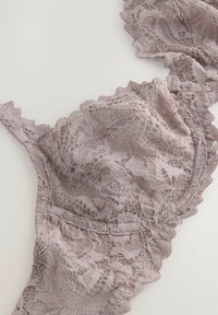 Hieno mauve pitsi rintaliivi, jossa on kukkakuviota ja aaltoilevia reunoja, asetettuna tasaiselle neutraalille pinnalle.