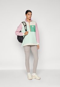 Lettet, farveblokeret pullover i pink, mint og beige med lynlås ved kraven og frontlomme; sat sammen med beige cargo bukser og sneakers.