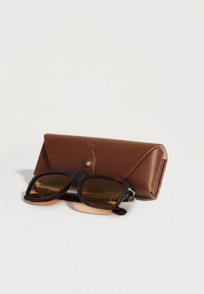 Καφέ δερμάτινη θήκη για γυαλιά με κλείσιμο με πάτημα και μαύρα ορθογώνια γυαλιά ηλίου με καφέ φακούς που ξεκουράζονται μπροστά.