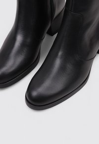 Botines de piel negra hasta el tobillo con punta afilada y tacón cuadrado. Textura lisa, costuras mínimas y cierre con cremallera lateral.