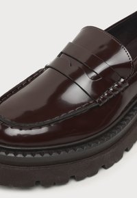 Mocassin en cuir brun foncé poli avec bout moc cousu et semelle épaisse en caoutchouc noir à crampons.