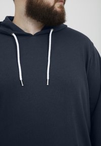 Sudadera azul marino oscura con cordón que presenta cintas blancas y puntas metálicas, hecha de una tela suave, con un corte relajado y sin patrones visibles.
