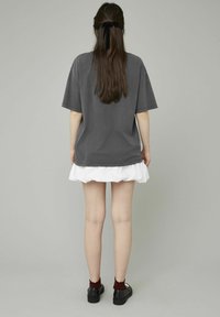 T-shirt gris surdimensionné avec des manches retroussées, superposé à une jupe blanche à volants. Chaussures noires avec des chaussettes bordeaux. Vue de dos.