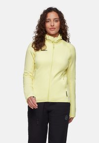 Helle gelbe Zip-Jacke aus dehnbarem Stoff. Sie verfügt über ein eng anliegendes Design, einen hohen Kragen und zwei seitliche Reißverschlusstaschen.