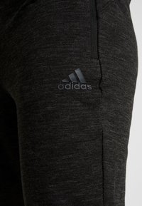 Schwarze Sporthose aus strukturiertem Material mit schlankem Schnitt. Verfügt über ein kleines, geprägtes schwarzes Adidas-Logo am unteren Bein.