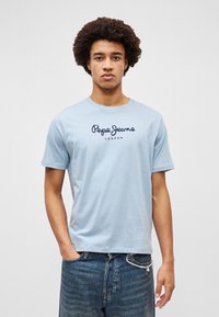 Ανοιχτό μπλε βαμβακερό μπλουζάκι με κοντά μανίκια, με λογότυπο και κείμενο "Pepe Jeans LONDON" μπροστά, σχήμα γύρου στον λαιμό, λεία υφή.