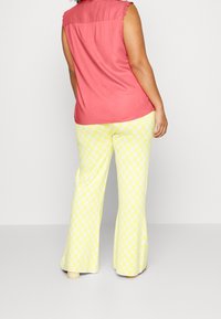 Krótki różowy top bez rękawów z koronkowymi akcentami, w połączeniu z żółtymi spodniami dzwonami z wzorem w serca.