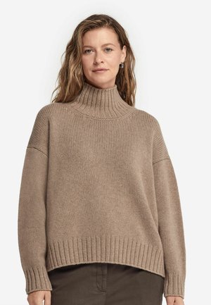 Beige polotröja med tjock ribbad textur, lös passform, nedhasade axlar och breda ärmslut. Har en hög krage och en rak fåll.
