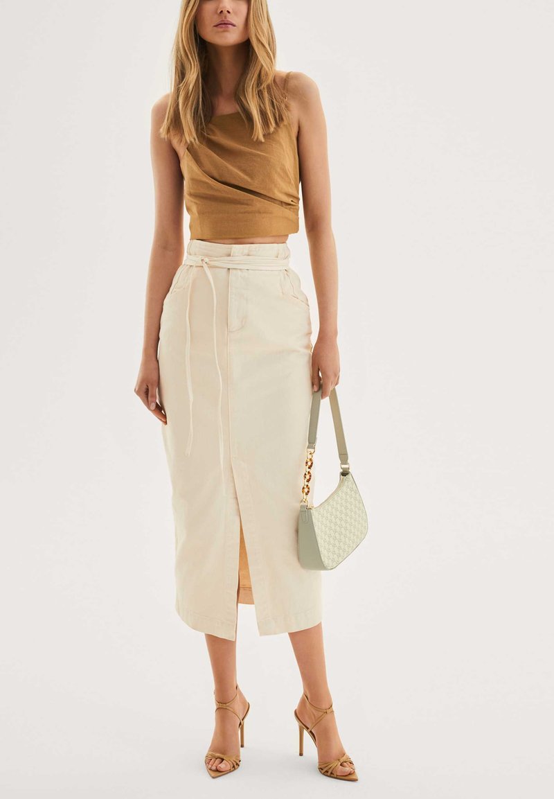 Barna crop top laza kialakítással, krém színű maxi szoknya elől hasítékkal és húzózsinórral. Világos zöld kézitáska mintás textúrával. Pántos magassarkú cipők.