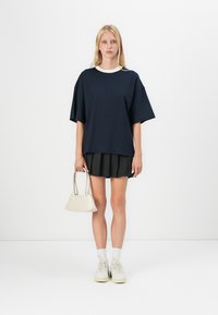 Námornícky oversized tričko s bielym golierom, čierna plisovaná sukňa, krémová kabelka, biele tenisky a biele ponožky do členkov. Jednoduchý dizajn a farby.