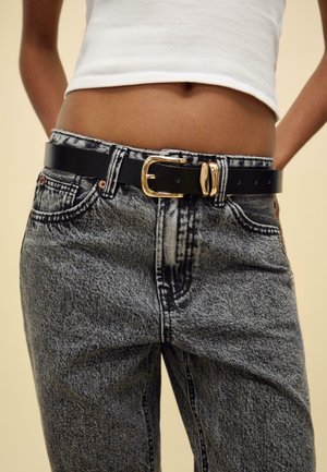 Svart konstläderbälte med ett guldspänne, bärs över högmidjade grå jeans i denim med en blekt tvätt och subtila sömdetaljer.