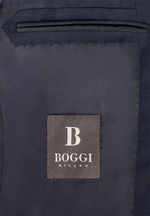 Marineblauem Stoff mit glatter Textur ist ein graues Etikett aufgenäht. Das Etikett zeigt das Logo "B" und den Text "BOGGI MILANO."