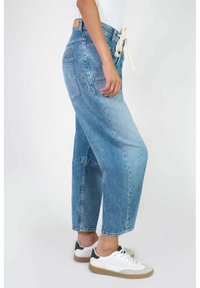 Jeans de mezclilla azul claro con corte suelto, que cuentan con bolsillos laterales, una cintura con cordón y un ligero desgaste. Combinados con zapatillas blancas.