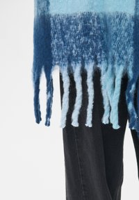 Strikket blå ombre-scarf med frynser, der har varierende nuancer fra mørk til lys blå, tekstureret fibre og en blød finish.