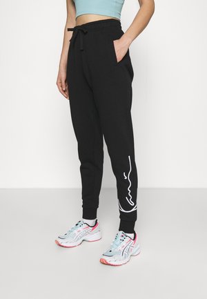 Personne portant un jogging noir avec un motif de lignes abstraites blanches sur le bas de la jambe, un haut court bleu clair et des chaussures de sport blanches.