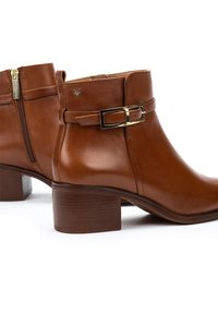Bottines en cuir marron avec un talon carré, une fermeture éclair sur le côté et une sangle décorative avec une boucle dorée. Texture lisse, design simple.