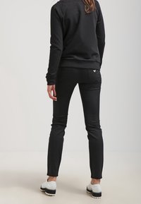 Svarta jeans med en slät textur och minimala sömmar, i kombination med en svart sweatshirt och vita skor med svarta sulor.