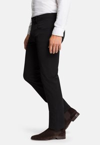 Black pants with a slim fit and five-pocket design, featuring contrast stitching, and worn with brown suede ankle boots.