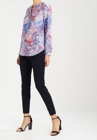 Long-sleeve shirt with a vibrant blue, pink, and white floral pattern, paired with slim black pants and black strappy heels.