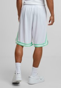 Shorts de sport blancs en tissu léger, avec des rayures accentuées vertes au niveau de l'ourlet, et une taille élastique pour un confort optimal.