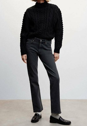 Suéter negro de punto con cuello alto, combinado con vaqueros rectos gris oscuro y mocasines negros, creando un conjunto monocromático.