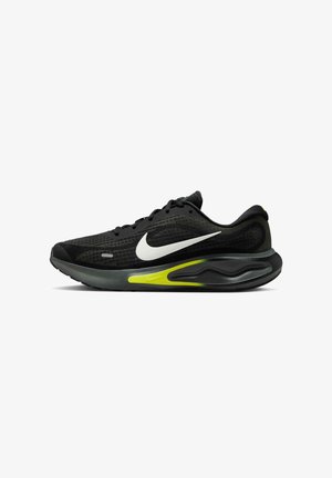 Chaussure de sport noire avec un upper en mesh, un swoosh Nike blanc et un accent vert sur la semelle. Design léger avec des surfaces texturées.