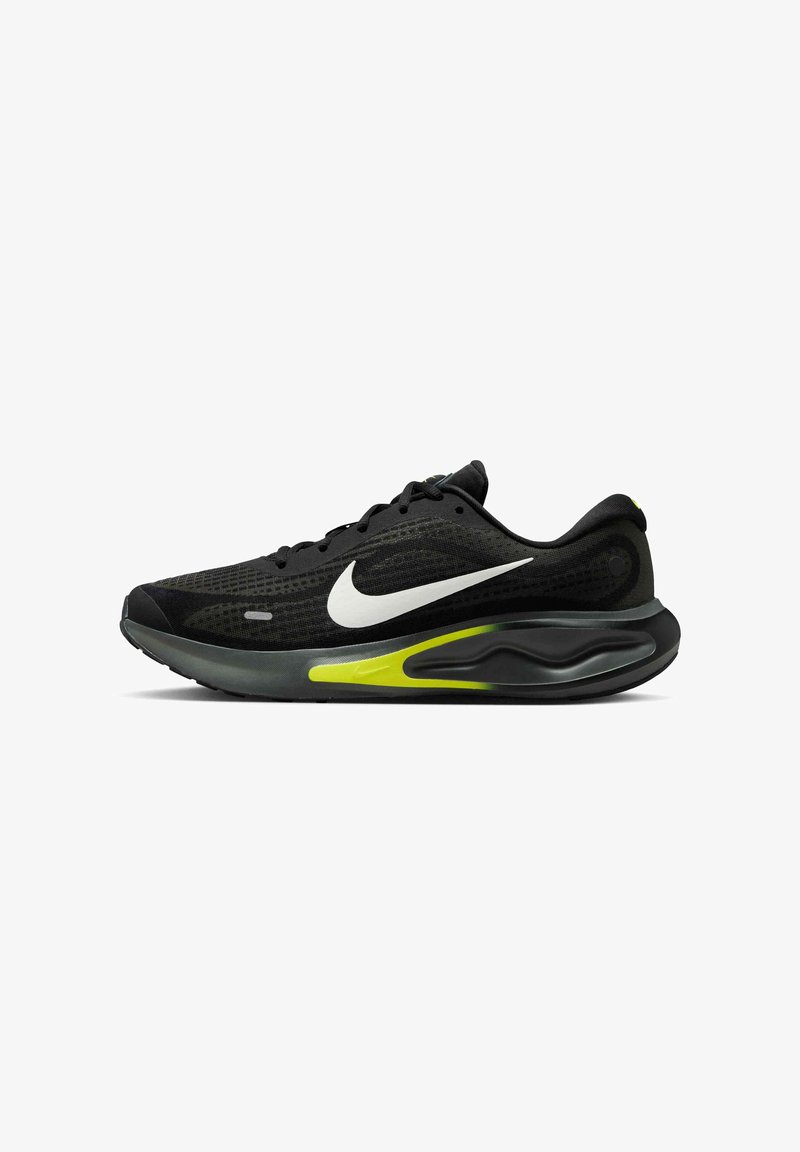 Scarpa sportiva nera con tomaia in rete, la caratteristica swoosh bianca di Nike e un accento verde sulla suola. Design leggero con superfici texture.