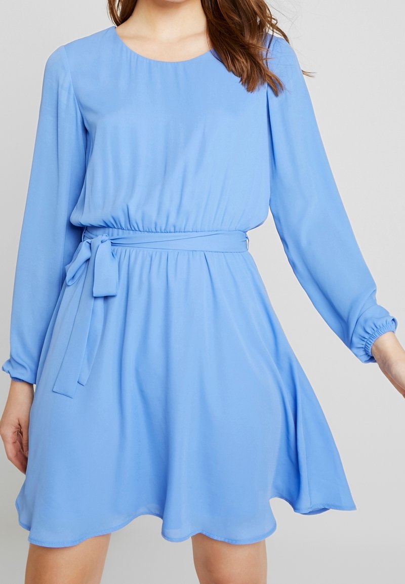 Ljusblå klänning med lång ärm, elastisk midja och bälte. Slätt tyg, utsvängd kjol med en subtil fåll.