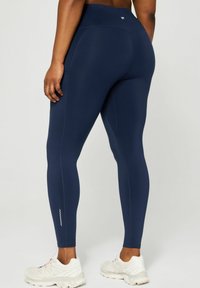 Navy blue leggings made from smooth, stretchy fabric with a high waistband, featuring white accent stripes at the ankles and minimal branding.