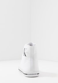Weiße High-Top-Sneaker aus Canvas-Material, mit einem schwarzen Logo "CK" und "CALVIN KLEIN JEANS" an der Ferse sowie einem einfachen schwarzen Streifen.