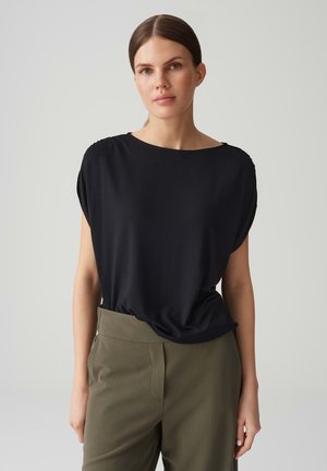 Zwarte losse top met een ronde halslijn en korte mouwen, gecombineerd met olijfgroene highwaisted broek. Zachte, gladde stofstructuur.