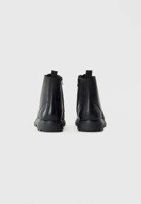 Botas negras hasta el tobillo hechas de cuero suave, con punta redondeada, lengüetas traseras y cremalleras laterales. Suela de goma para mayor tracción.