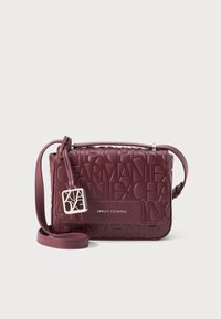 Geantă crossbody burgundy cu design de logo embossat, suprafață texturată, curea împletită și etichetă din metal de culoare argintie.